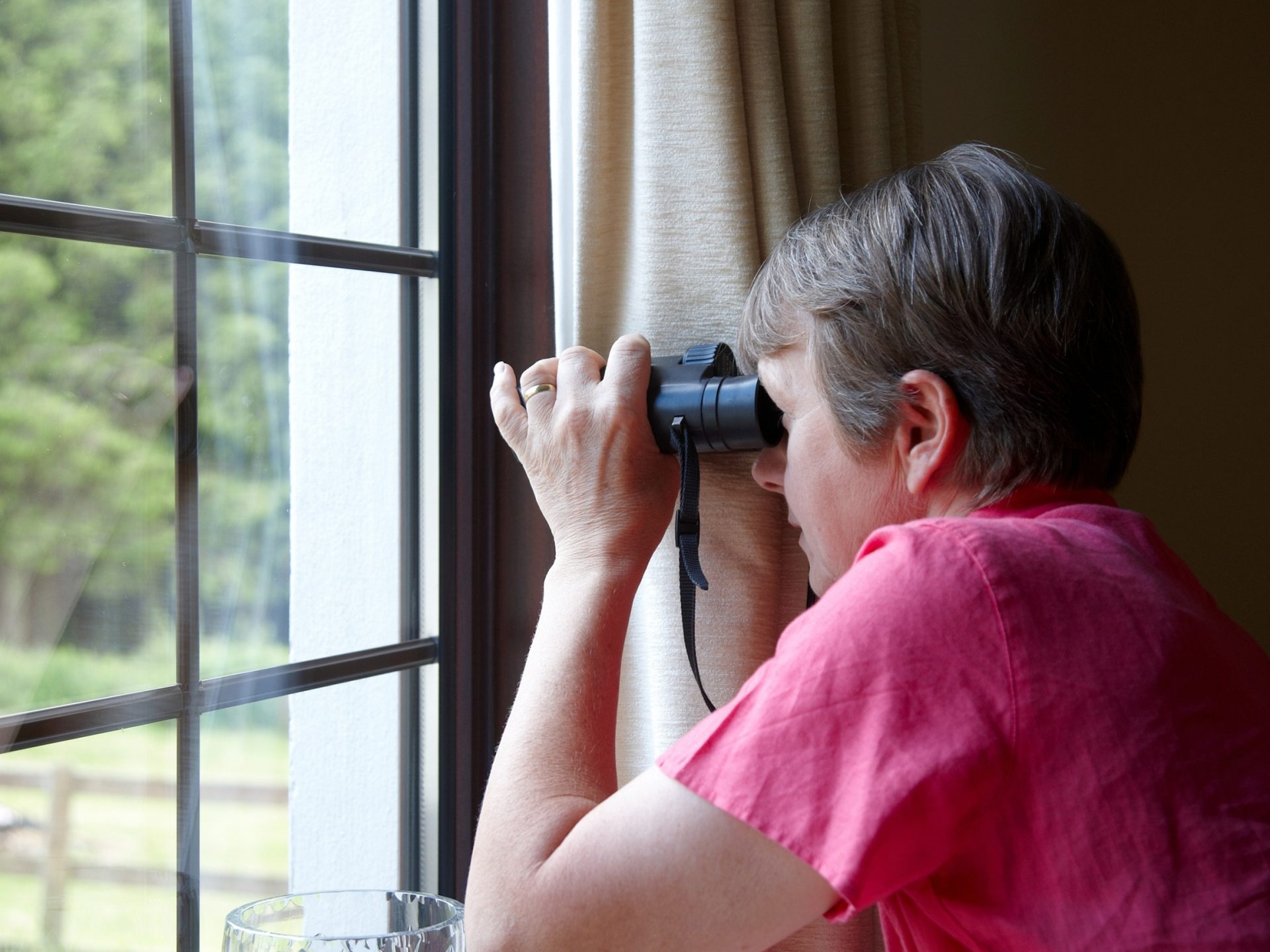 Woman looking out window with binoculars