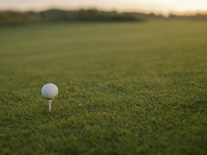 Golf ball on a white tee at sunrise on a golf course fairway