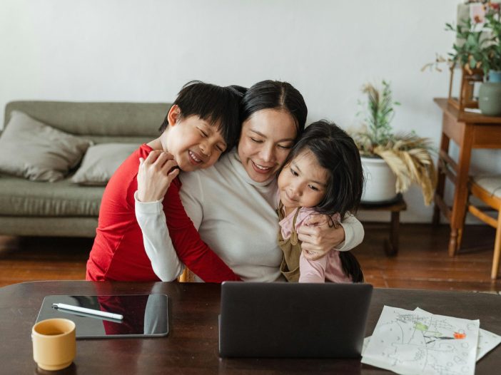 A parent hugs two young children while sitting at a table