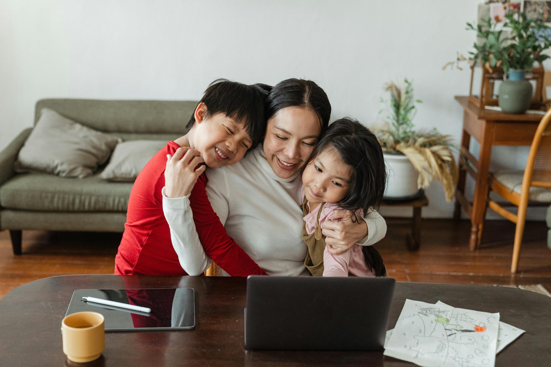 A parent hugs two young children while sitting at a table