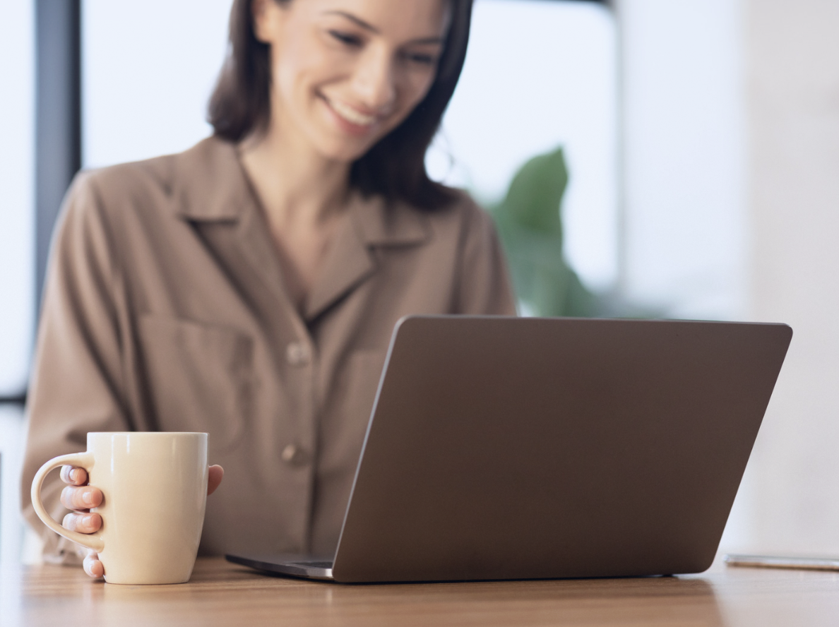 Person using a laptop while holding a coffee mug at a desk.