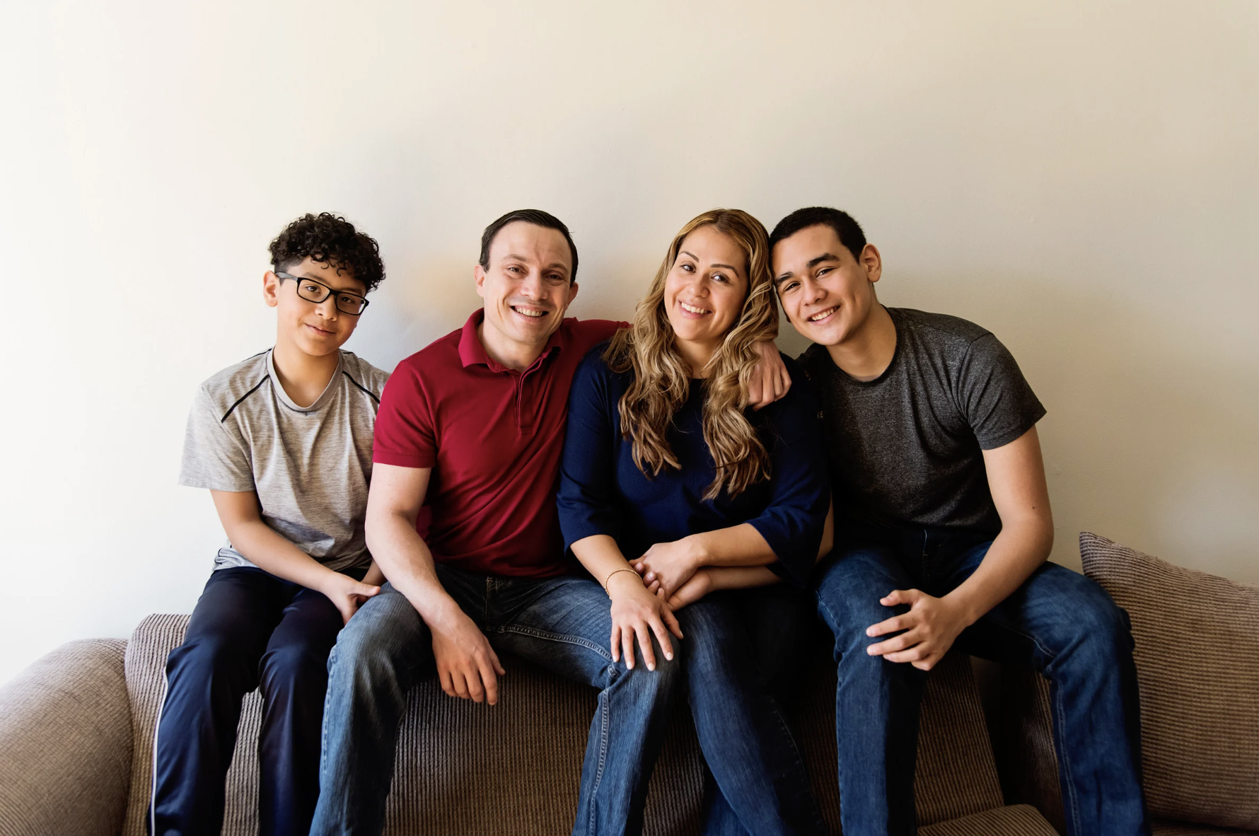 Two adults and two older children sitting together on a couch, smiling indoors.