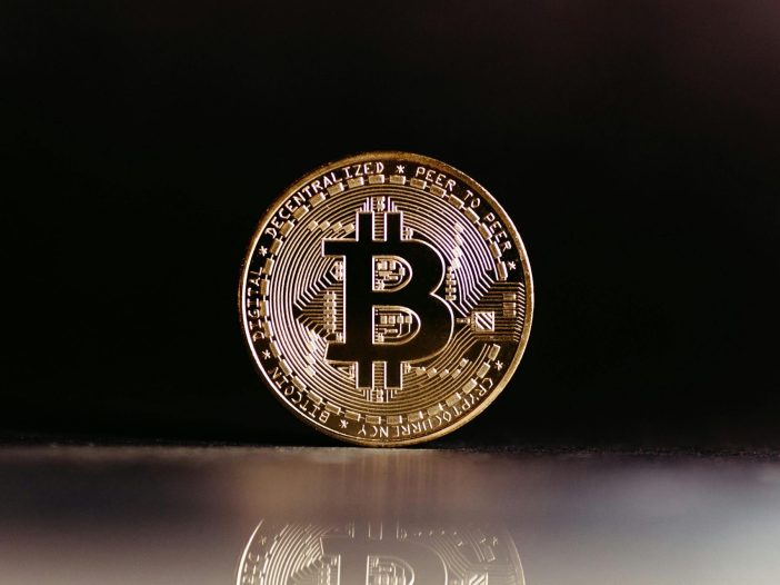 Gold Bitcoin coin standing upright on a dark reflective surface