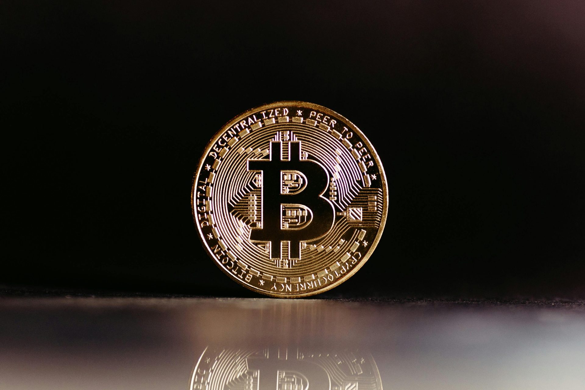 Gold Bitcoin coin standing upright on a dark reflective surface