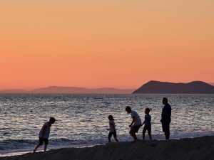 A group of adults and children walking together along a beach at sunset