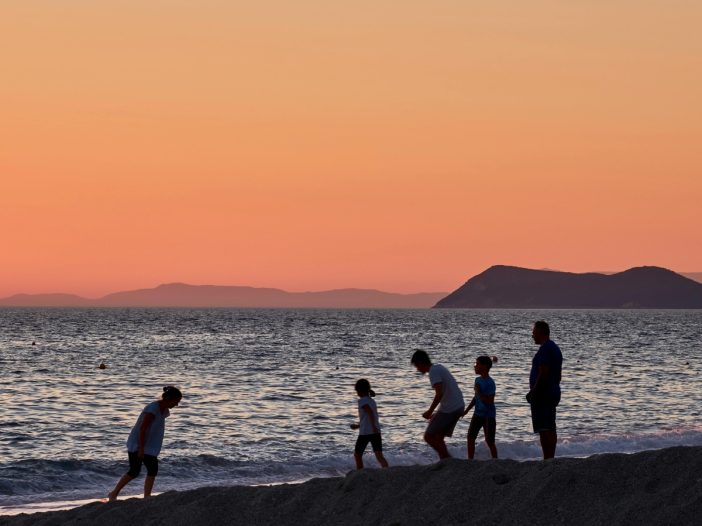 A group of adults and children walking together along a beach at sunset