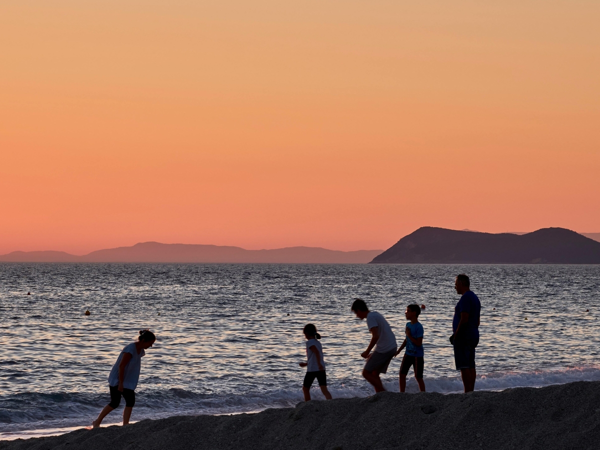 A group of adults and children walking together along a beach at sunset