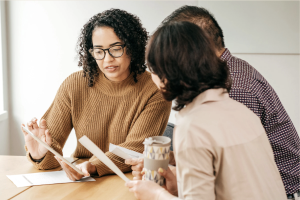 A financial advisor reviewing documents on a tablet with two clients seated at a table