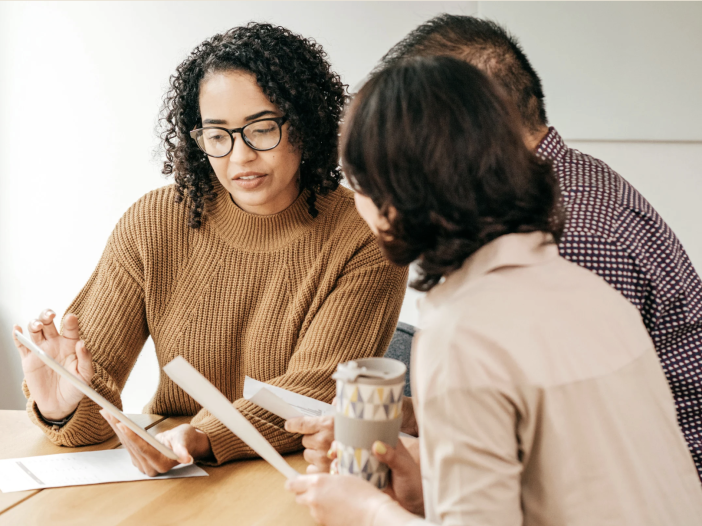 A financial advisor reviewing documents on a tablet with two clients seated at a table