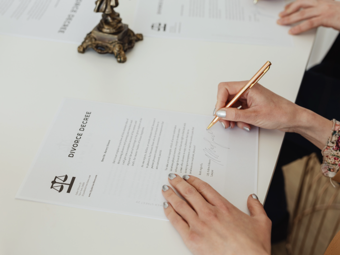 Person signing a divorce decree document on a white desk with legal papers in the background