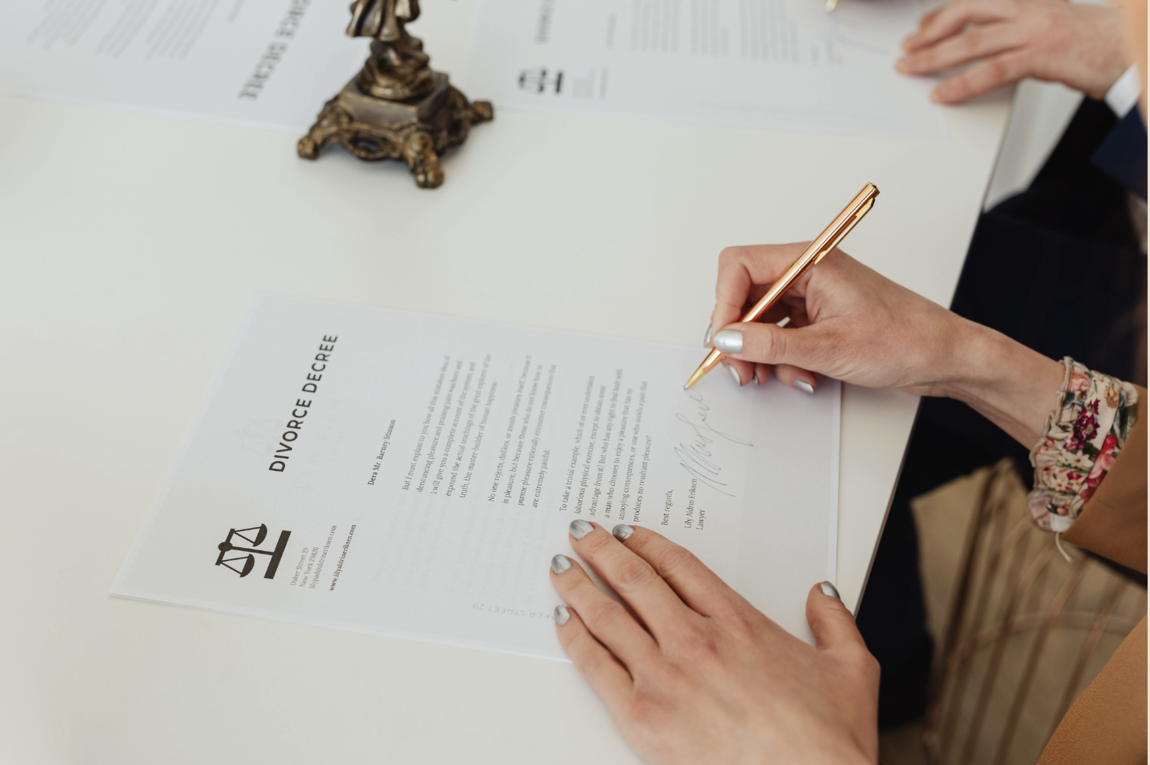 Person signing a divorce decree document on a white desk with legal papers in the background