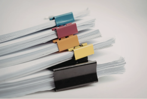 Stacks of white paper documents secured with colorful binder clips on a light gray surface