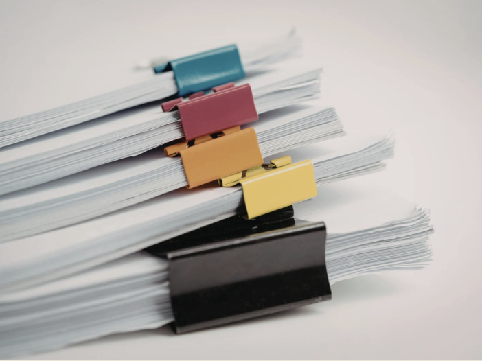 Stacks of white paper documents secured with colorful binder clips on a light gray surface
