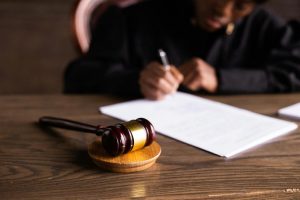 Alabama probate judge in black robe signing documents at a wooden desk with a gavel in the foreground