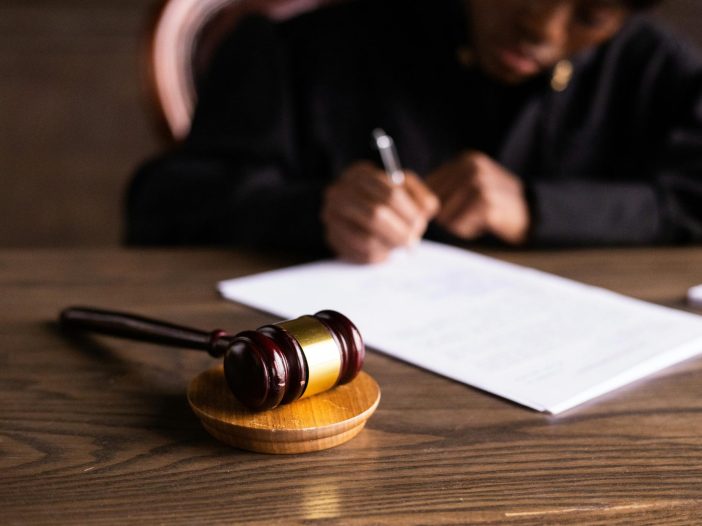 Alabama probate judge in black robe signing documents at a wooden desk with a gavel in the foreground