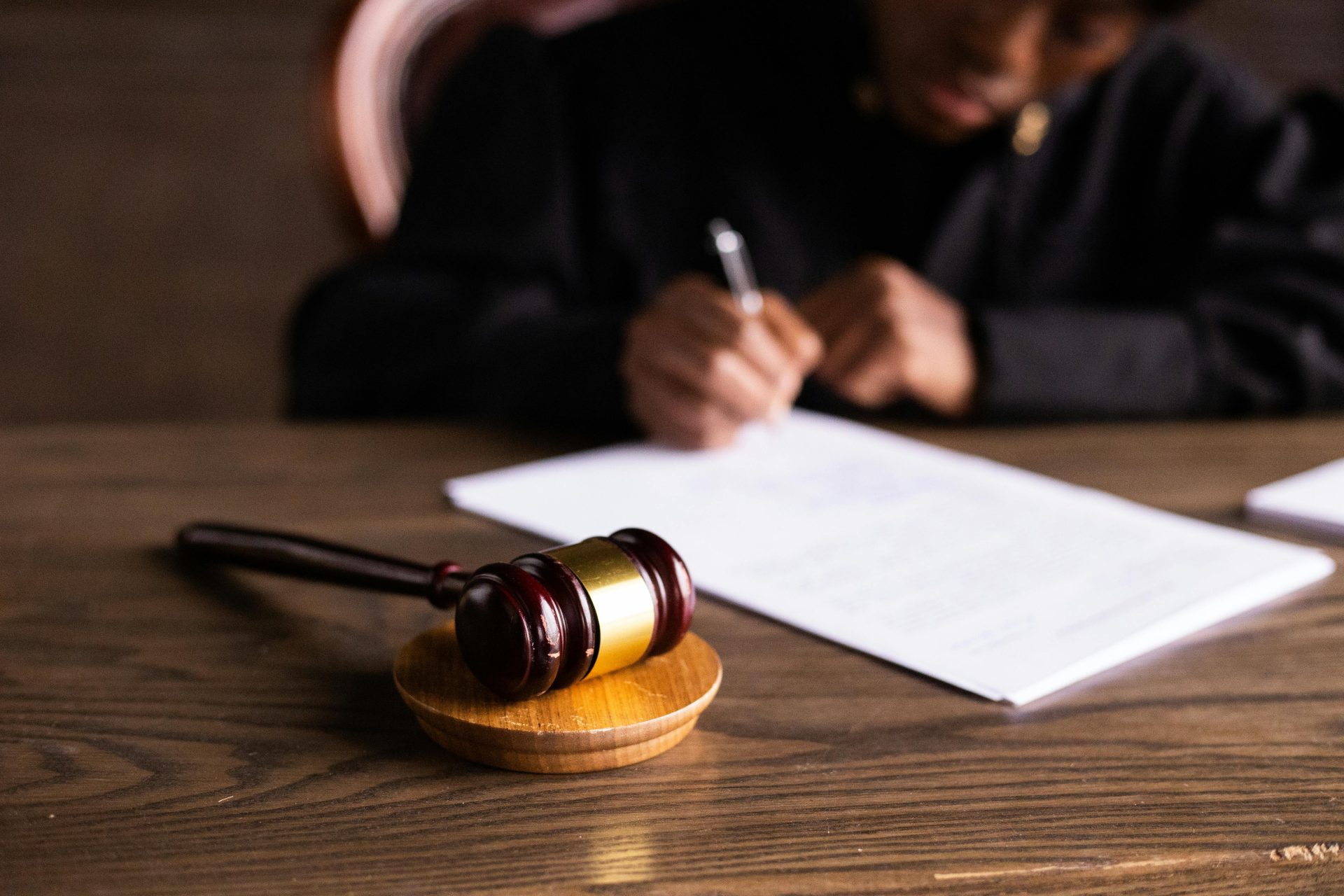 Alabama probate judge in black robe signing documents at a wooden desk with a gavel in the foreground