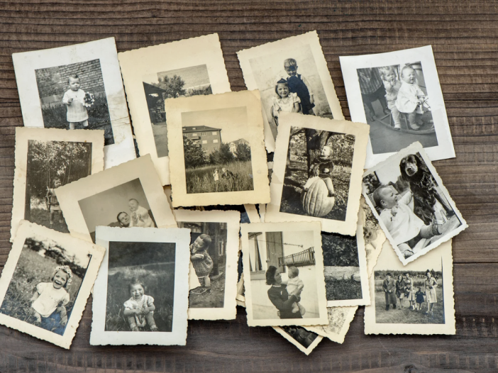 Pile of old black and white family photographs spread out on a dark wooden table