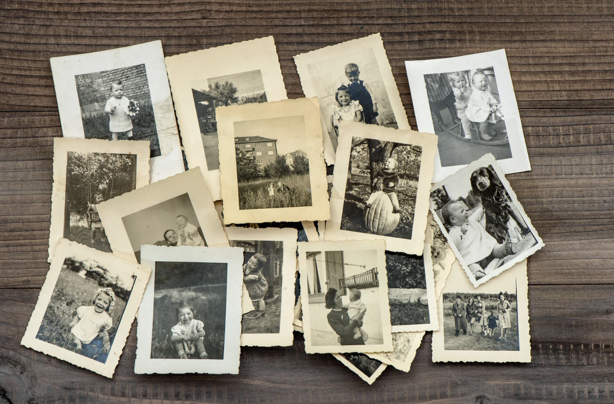 Pile of old black and white family photographs spread out on a dark wooden table