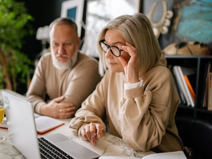 Older couple sitting together at a table, reviewing an online will on a laptop