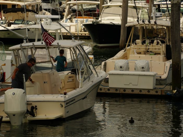 Father and son cleaning a Grady-White boat together at a crowded marina, American flag flying from the bow