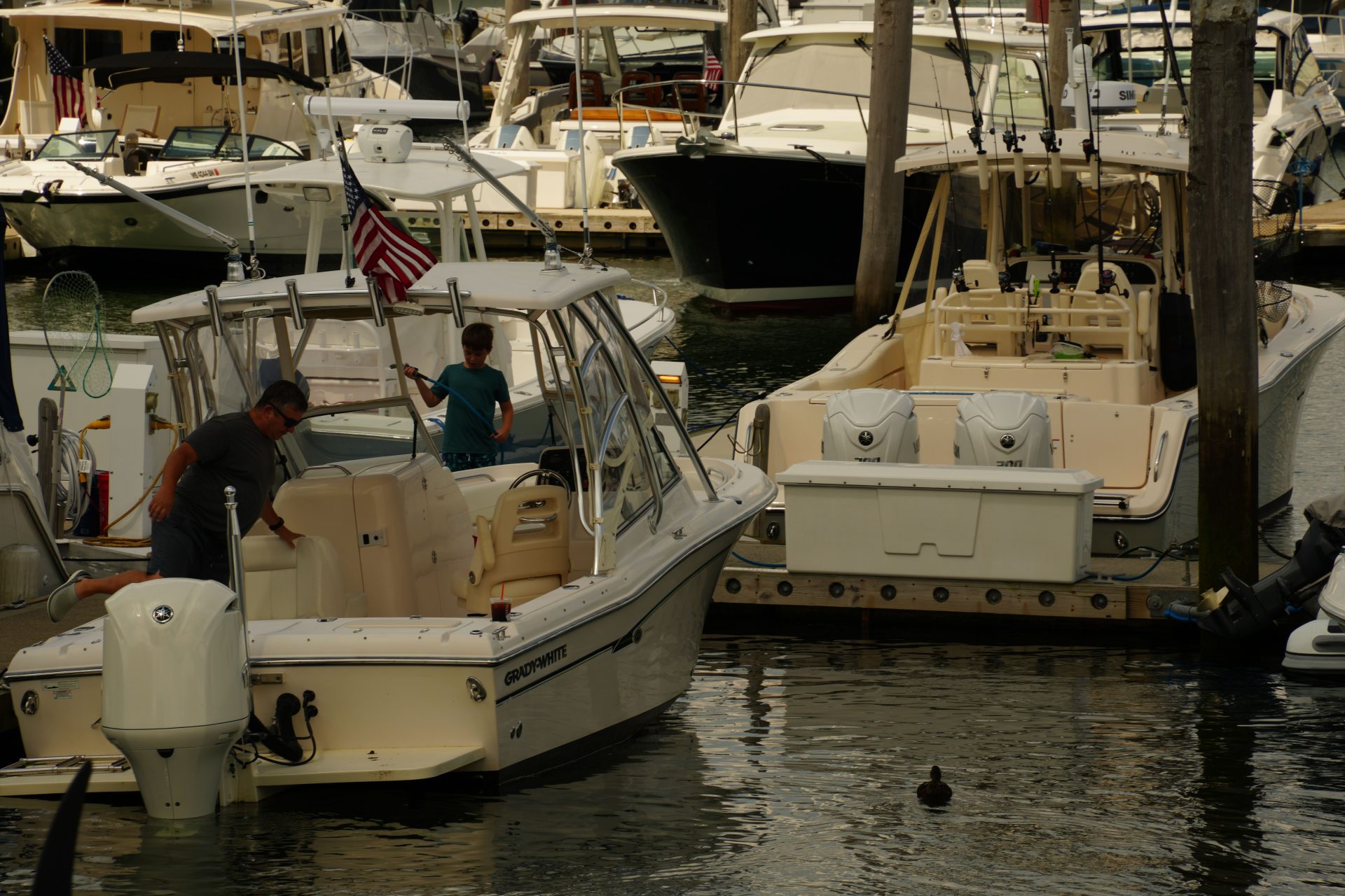 Father and son cleaning a Grady-White boat together at a crowded marina, American flag flying from the bow