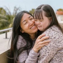 Mother embracing her adult daughter with Down syndrome on an outdoor rooftop balcony