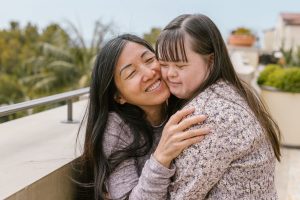 Mother embracing her adult daughter with Down syndrome on an outdoor rooftop balcony