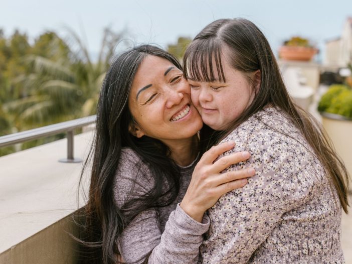 Mother embracing her adult daughter with Down syndrome on an outdoor rooftop balcony