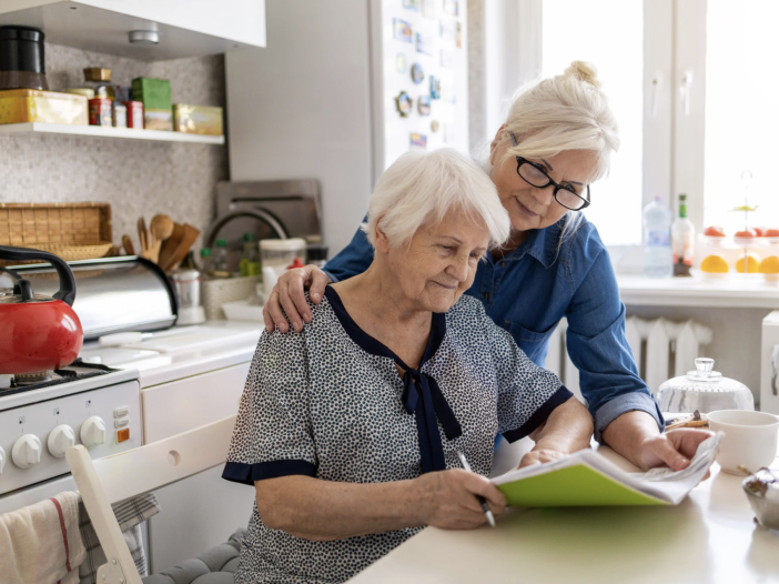 Older mother and adult daughter sitting together reviewing documents at a kitchen table