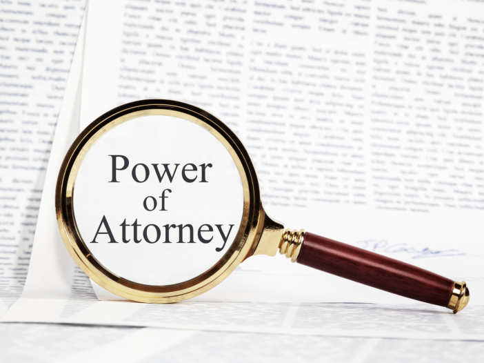 A gold magnifying glass with a wooden handle rests on a signed legal document, magnifying the words “Power of Attorney.” The image illustrates the scrutiny and oversight that can help prevent power of attorney abuse in Alabama.