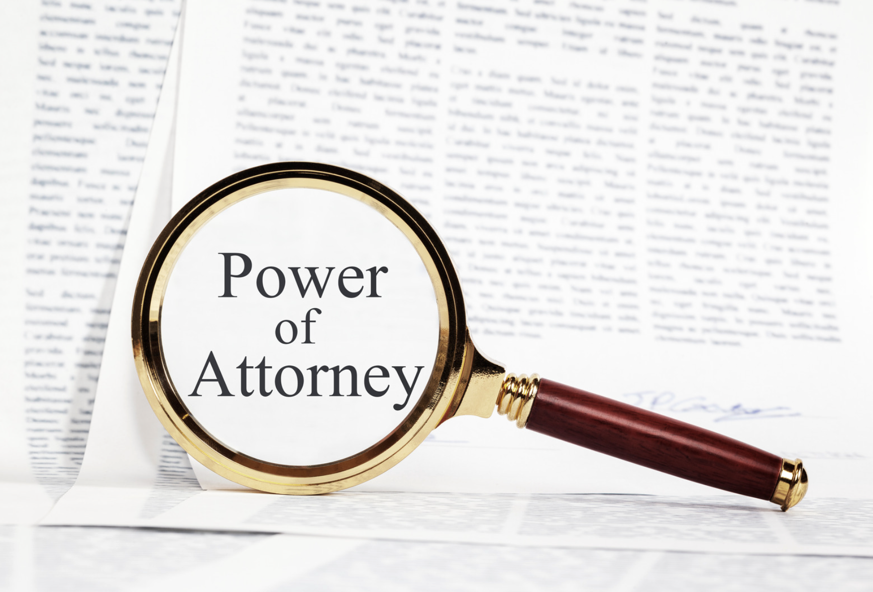 A gold magnifying glass with a wooden handle rests on a signed legal document, magnifying the words “Power of Attorney.” The image illustrates the scrutiny and oversight that can help prevent power of attorney abuse in Alabama.