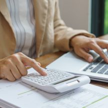Person using a calculator and laptop at a desk with financial documents, with text asking what a trustee owes the beneficiaries