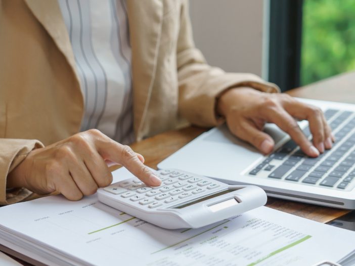 Person using a calculator and laptop at a desk with financial documents, with text asking what a trustee owes the beneficiaries
