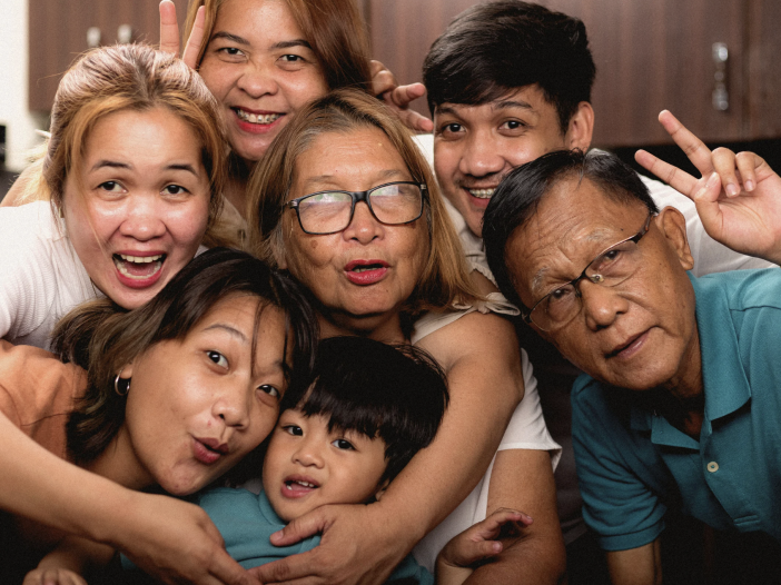 Three generations of a family, including grandparents, adult children, and a young boy, smiling and posing close together indoors