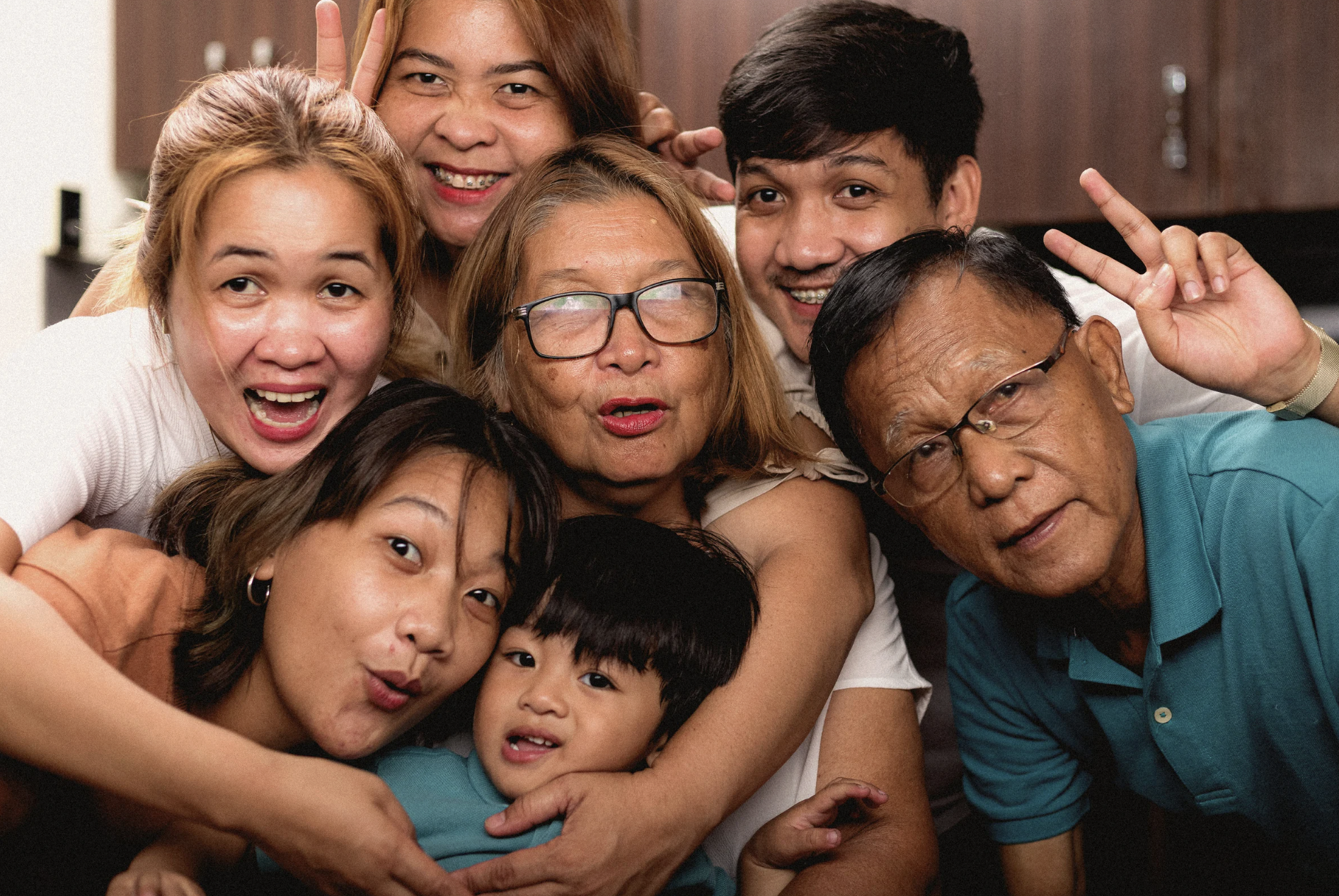 Three generations of a family, including grandparents, adult children, and a young boy, smiling and posing close together indoors